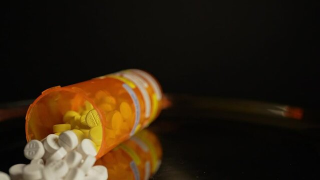 Prescription pill bottle falling at the table and scatter medications in slow motion. Opioid crisis in America, narcotic addiction and overdoses by substance abuse.