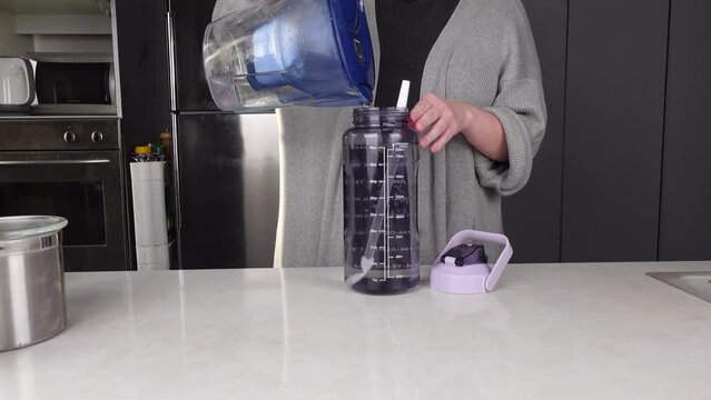 Woman pours filtered water into a reusable bottle from a pitcher, promoting eco-conscious hydration choices and reusable bottle. Stay hydrated concept. 