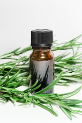 rosemary essential oil in a yellow glass bottle and rosemary sprigs on a white background