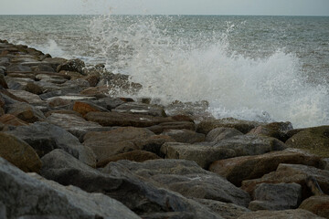 The strong wave hits the rock dam with seascape background