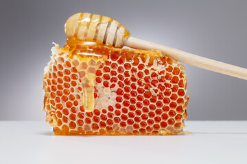 Honeycomb with flowing honey on a gray background. Honey pouring from honey stick on a honeycomb....