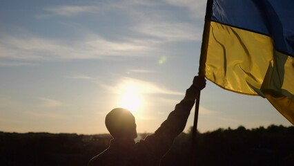 Male soldier stands with raised flag of Ukraine against background of beautiful sunset. Male...