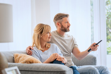 Mid aged woman and man sitting at home and watcing tv together