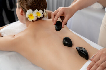 Obraz na płótnie Canvas Hot stone massage at spa salon in luxury resort with day light serenity ambient, blissful woman customer enjoying spa basalt stone massage glide over body with soothing warmth. Quiescent
