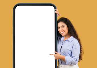 Cheerful young woman in a blue shirt peeks out from behind a large smartphone