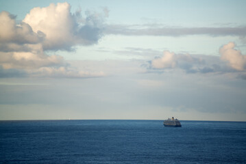 Blue sea with a cruise ship going into the distance and pink clouds in the sky - 709256056