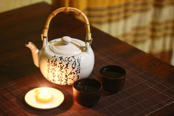 Chinese teapot with hieroglyphs, small clay tea cups in an ethnic atmosphere on a candlelit table.