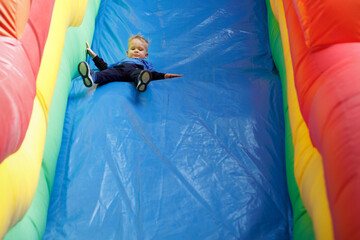 A little scared child sliding down an a blue inflatable slide. There is free space for text in the image