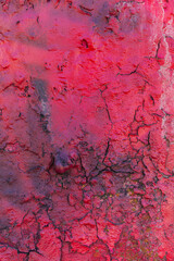 A crimson red, shiny, uneven, chipped, and cracked old concrete wall. The layer texture with black cracks is interesting