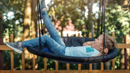 Relaxing in a hammock. A cheerful little boy swings with his leg up - obrazy, fototapety, plakaty