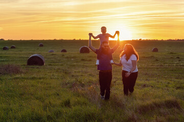 A close-knit family is having fun in a rural wide grass field in the sunset sunlight.