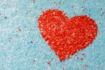 The shape of a red heart on a light blue background is made of colored sand crystals.