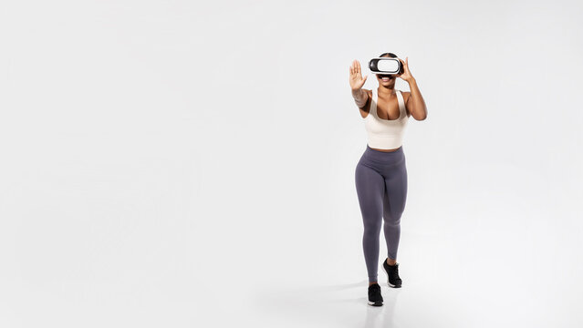 Sporty black lady experiencing virtual reality training on white backdrop