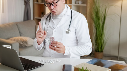 Pills consulting. Health video appointment. Doctor man in white uniform explaining tablets medication effect at laptop meeting sitting at workplace desk.