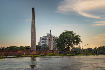 Obraz premium brick chimney, tree, building and clear sky at the bank of the river