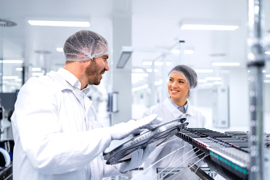 Factory workers operating advanced semiconductor production machine in automotive industry.