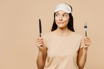 Young hungry Latin woman she wears pyjamas jam sleep eye mask rest relax at home hold fork spoon...