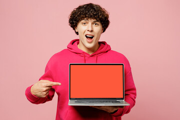 Young Caucasian IT man wear hoody casual clothes hold use work on blank screen workspace area point index finger on laptop pc computer isolated on plain pastel light pink background Lifestyle concept