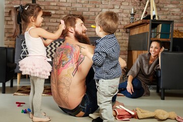 Children playing with father at home, combing hair, colouring his back. - obrazy, fototapety, plakaty