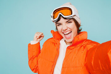 Close up winner skier young woman wears padded jacket hat ski goggles mask do selfie shot on mobile cell phone travel rest spend weekend winter season in mountains isolated on plain blue background.