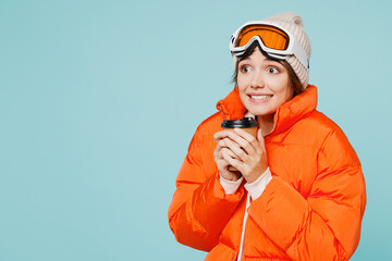 Skier sad young woman in padded windbreaker jacket hat ski goggles mask hold takeaway delivery cup coffee to go travel rest spend weekend winter season in mountains isolated on plain blue background