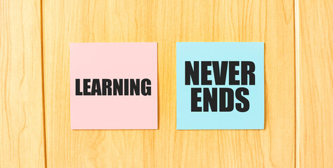 Inscription LEARNING NEVER ENDS on pink and blue square sticky sticker on wooden wall