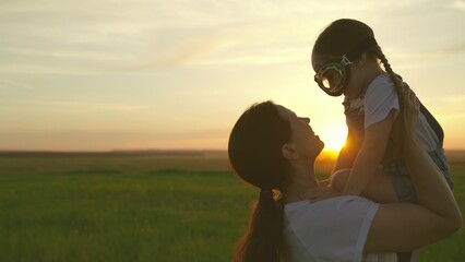 Little girl smiles, plays with his mother in outdoor. Happy family. Child plays pilot, dream is to...