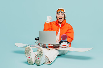 Full body winner young IT woman in windbreaker jacket hat ski goggles mask sit with snowboarding...