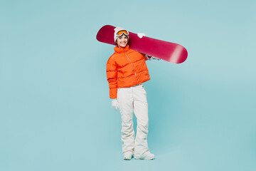 Full body happy young woman wear warm padded windbreaker jacket hat ski goggles mask hold snowboard on shoulder travel rest spend weekend winter season in mountains isolated on plain blue background. © ViDi Studio