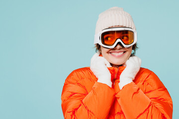 Fototapeta na wymiar Close up young smiling cheerful skier woman wear warm padded windbreaker jacket hat ski goggles mask look aside travel rest spend weekend winter season in mountains isolated on plain blue background.