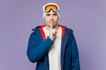 Skier man wear warm blue windbreaker jacket ski goggles mask say hush be quiet, finger on lips shhh gesture spend weekend winter season in mountains isolated on plain purple background. Hobby concept.