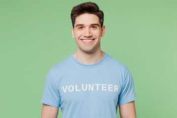 Young smiling fun happy cheerful man he wears blue t-shirt white title volunteer look camera isolated on plain pastel light green background. Voluntary free work assistance help charity grace concept.