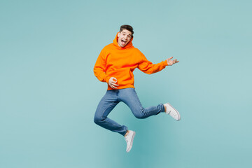 Full body happy singer young man he wears orange hoody casual clothes jump high play do air guitar gesture isolated on plain pastel light blue cyan color background studio portrait. Lifestyle concept. - obrazy, fototapety, plakaty