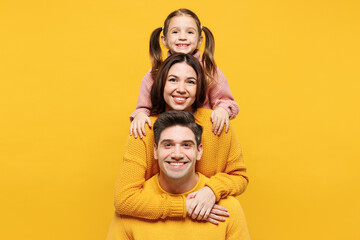 Fototapeta na wymiar Young happy smiling cheerful parents mom dad with child kid girl 7-8 years old wear pink knitted sweater casual clothes stand behind each other isolated on plain yellow background. Family day concept.