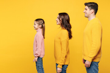 Side profile view young Caucasian happy cool parents mom dad with child kid girl 7-8 years old wearing pink knitted sweater casual clothes isolated on plain yellow wall background. Family day concept.