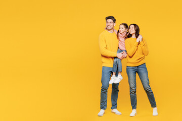 Full body young happy parents mom dad with child kid girl 7-8 years old wear pink sweater casual clothes hold little daughter look aside on area isolated on plain yellow background Family day concept