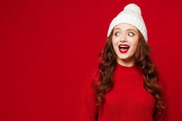 Young surprised impressed amazed shocked Caucasian woman she wears knitted sweater white hat casual clothes look aside on area isolated on plain red color background studio portrait Lifestyle concept