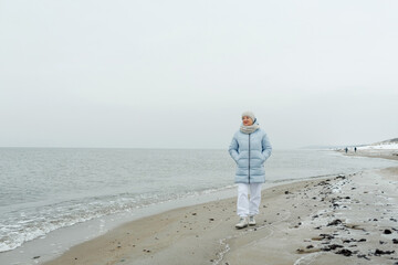 A beautiful elderly woman enjoys a frosty day while walking along the beach