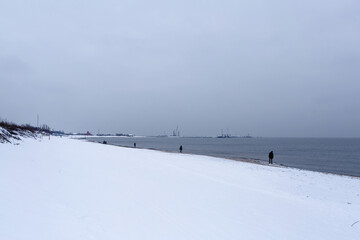 There is snow on the seashore, people are walking in the distance