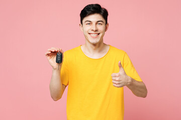 Young fun Caucasian man he wears yellow t-shirt casual clothes hold in hand car key fob keyless system show thumb up isolated on plain pastel light pink background studio portrait. Lifestyle concept.