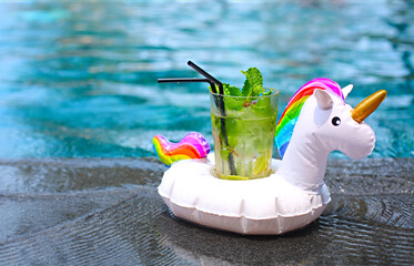 Mojito cocktail at the edge of a resort pool in inflatable unicorn. Concept of luxury vacation