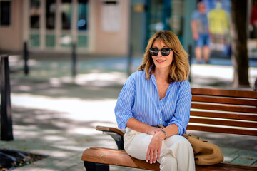 Blond haired woman sitting on a bench in the city and waiting for somebody