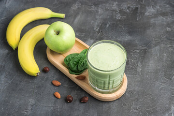 Green detox smoothie in a glass, blended vegetarian drink from spinach leaves, apple, banana fruit...