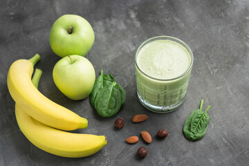Green detox smoothie in a glass, blended vegetarian drink from spinach leaves, apple, banana fruit and nuts on dark background, healthy eating concept