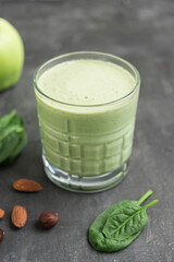 Green detox smoothie in a glass, blended vegetarian drink from spinach leaves, apple, banana fruit and nuts on dark background, healthy eating concept