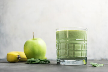 Green detox smoothie in a glass, blended vegetarian drink from spinach leaves, apple and banana...