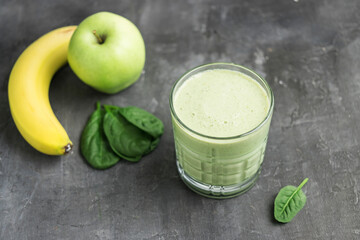 Green detox smoothie in a glass, blended vegetarian drink from spinach leaves, apple and banana fruit on dark background, healthy eating concept