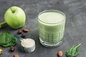 Green detox smoothie in a glass, measuring spoon with protein powder, blended vegetarian drink from...