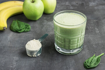 Green detox smoothie in a glass, measuring spoon with protein powder, blended vegetarian drink from...