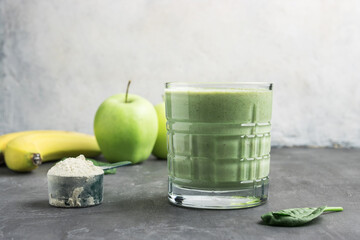 Green detox smoothie in a glass, measuring spoon with protein powder, blended vegetarian drink from...